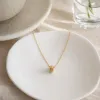 A golden cylindrical small diamond pendant necklace with a white card attached to a transparent bag details Picture